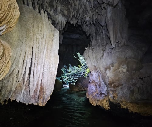 View through a limestone cave opening toward flowing water and daylight outside.