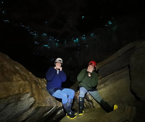 Private tour with visitors seated on a rock ledge beneath glowworms, highlighting the cave’s natural ceiling covered with glowworms