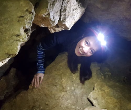 Visitor smiling while moving through a narrow limestone passage inside a Waitomo cave.